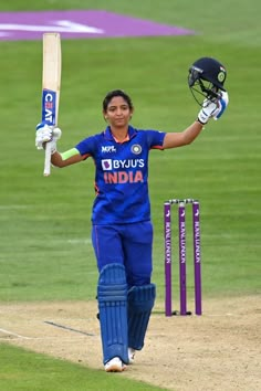 a female cricket player is holding her bat and helmet in the air as she walks off the field