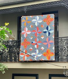 a large quilt hanging from the side of a building next to two doors and a balcony