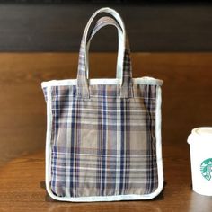 a starbucks coffee cup next to a plaid bag on a wooden table with a starbucks logo in the background