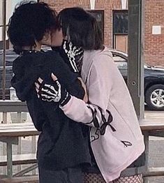 two people standing next to each other with their arms around one another and kissing in front of a building