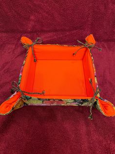 an orange tray on a red blanket with decorative handles and ties around the edge, sitting on top of a purple surface