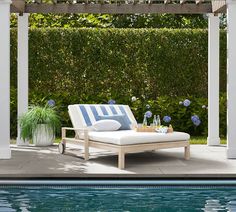 an outdoor lounge chair next to a pool with blue flowers and greenery in the background