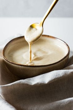 a spoon full of white sauce being drizzled on top of a bowl