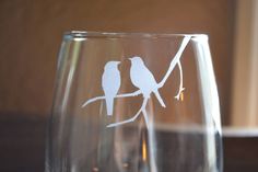 two birds are sitting on a branch in a wine glass that is etched with white ink