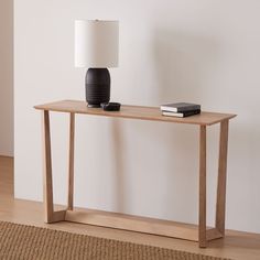 a wooden table with a lamp and books on it next to a white wall in an empty room