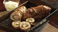 a roasting pan filled with sliced meat and vegetables next to a glass of dressing