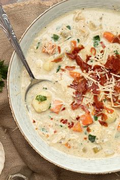 a white bowl filled with soup and bacon on top of a brown place mat next to silverware