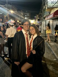 a man and woman in graduation gowns standing next to each other on the street