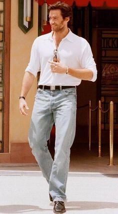 a man in white shirt and jeans walking down the street