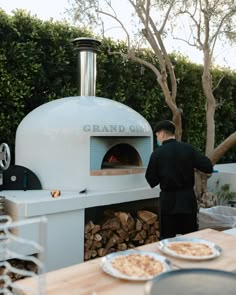 a man standing in front of an outdoor pizza oven