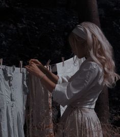 a woman is hanging out her clothes on a line in the woods while looking at them