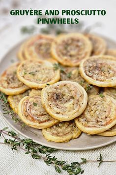 a plate full of mini pastries with herbs on top and the words gruyre and prosciutto pinwheels above it