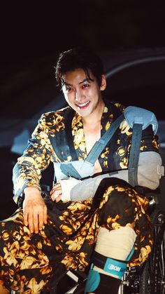 a man sitting on top of a wheel chair wearing a flower print shirt and pants