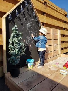 a young child is drawing on the side of a wooden wall next to a potted plant