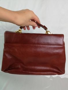 "Vtg leather cognac brown/reddish brown handbag with handle. Golden tone closure. Briefcase bag. Women`s retro purse. Inside brown vegan leather lining, 3 large compartments and 1 zip compartment. materials: leather shell; vegan leather lining condition: great vintage. The closure works well. Without serious damages. Some streaks on the leather surface (maybe 3 small). measurements: bottom width 32,5 cm / 12.7\" in height without handle 22,5 cm / 8.8\" in thickness 12 cm / 4.7\" in handle drop 1 Retro Leather Box Bag With Top Handle, Retro Leather Top Handle Box Bag, Retro Brown Satchel With Hasp Closure, Classic Brown Box Bag With Top Handle, Classic Brown Box Bag With Top Carry Handle, Retro Cognac Satchel Bag, Vintage Brown Shoulder Bag For Office, Retro Business Shoulder Bag With Detachable Handle, Brown Briefcase With Detachable Handle For Office