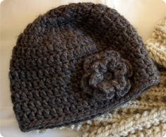 two crocheted hats are laying on top of each other, one is brown and the other is white