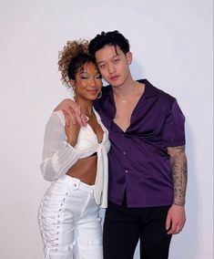 two people standing next to each other in front of a white wall and posing for the camera