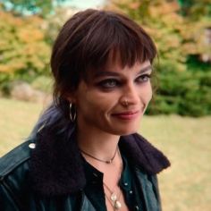 a woman with dark hair and piercings wearing a leather jacket smiling at the camera