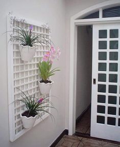 three white planters are hanging on the side of a wall with flowers in them