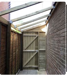 an alley way with brick walls and wooden doors leading to the back door, which has a glass roof over it