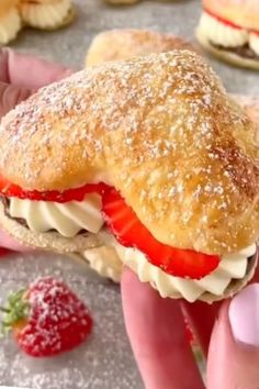 a person is holding a sandwich with strawberries on it and other pastries in the background