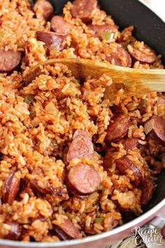 a pan filled with rice and sausages on top of a wooden spoon in it