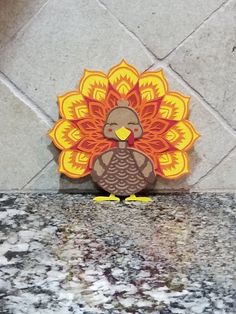 a turkey with an orange and yellow design on it's head sitting on a granite countertop