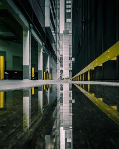 an empty city street with tall buildings reflected in the wet ground and yellow lines on the wall