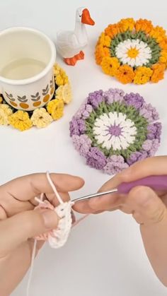 someone crocheting flowers on the table next to a coffee cup and mug holder