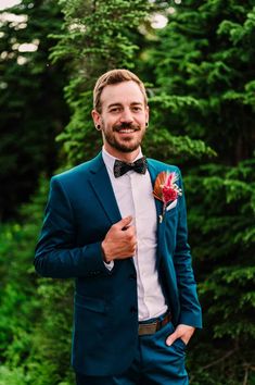 a man in a blue suit and bow tie is smiling at the camera with trees behind him