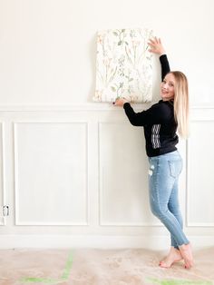 a woman is standing in front of a wall holding up a piece of fabric with flowers on it