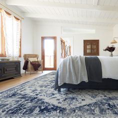 a bedroom with a bed, dresser and rug on the floor in front of it