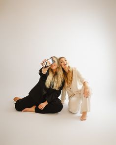 two women are sitting on the floor and one is taking a photo with her cell phone