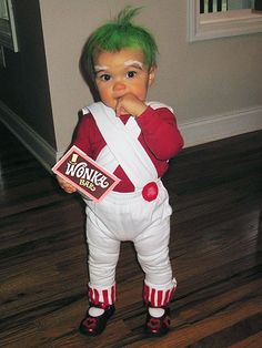 a young child with green hair and white overalls holding a candy bar in his hand