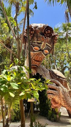 a wooden sculpture in the shape of a face surrounded by palm trees and greenery