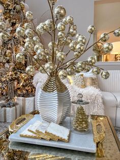 a table topped with gold and white christmas decorations on top of a silver tray next to a tree