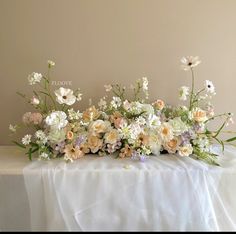 an arrangement of flowers on a table with white linens and a wall in the background