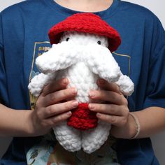 a person holding a white stuffed animal with red hat on it's head and wearing a blue t - shirt