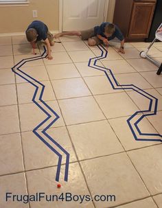 two boys are playing with blue tape on the floor