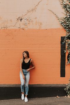 a woman leaning against a wall with her hand on her hip