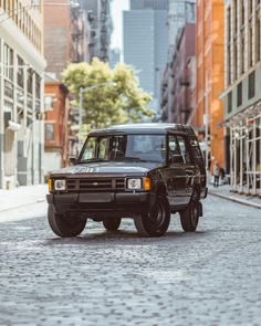 a black suv parked on the side of a street next to tall buildings in an urban setting