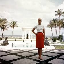 a woman standing in front of a pool with palm trees and water fountain behind her