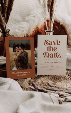 save the date cards are sitting on a bed with feathers in front of them and an image of a couple kissing