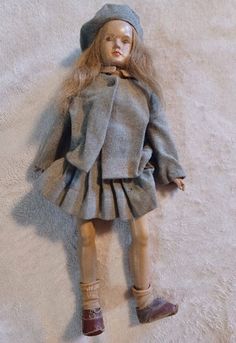 a doll is laying on the floor wearing a gray dress and hat with brown shoes