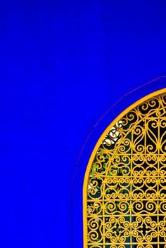 an orange and yellow clock on the side of a blue building with ironwork around it