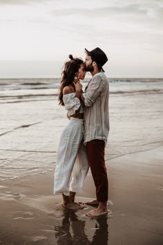 a man and woman standing next to each other on a beach near the ocean with their arms around each other