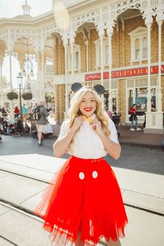 a woman in mickey mouse ears and red skirt posing for a photo on the street