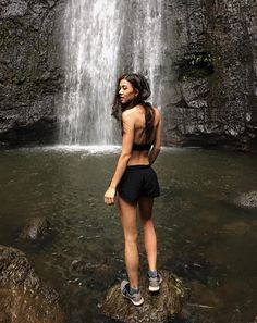 a woman standing in front of a waterfall with her back to the camera and looking up