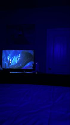 there is a television in the dark with blue lights on it's screen and a person sitting at the end of the bed