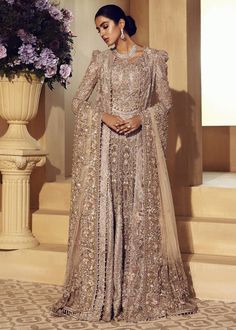 a woman standing in front of stairs wearing a long dress with an intricate pattern on it